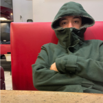 Chris sitting in chair with hoodie zipped up, half-covering his face
