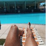 view of bare legs on lawn chair facing pool