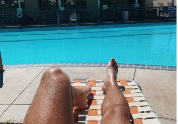 view of bare legs on lawn chair facing pool