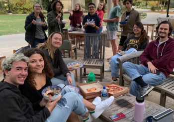 group of students sitting in chairs outside eating pizza