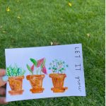 grass in background with hand holding card with painting of flower pots