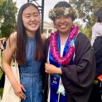 Emily with friend Amy in graduation robe and lei and flower crown