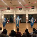 3 people in shark costumes dancing in front of a crowd